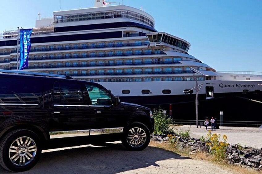 A large cruise ship docked at a port with a black SUV parked nearby. 2