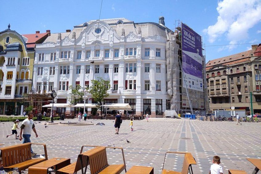 A public square with a historic building, benches, and a few people. 4