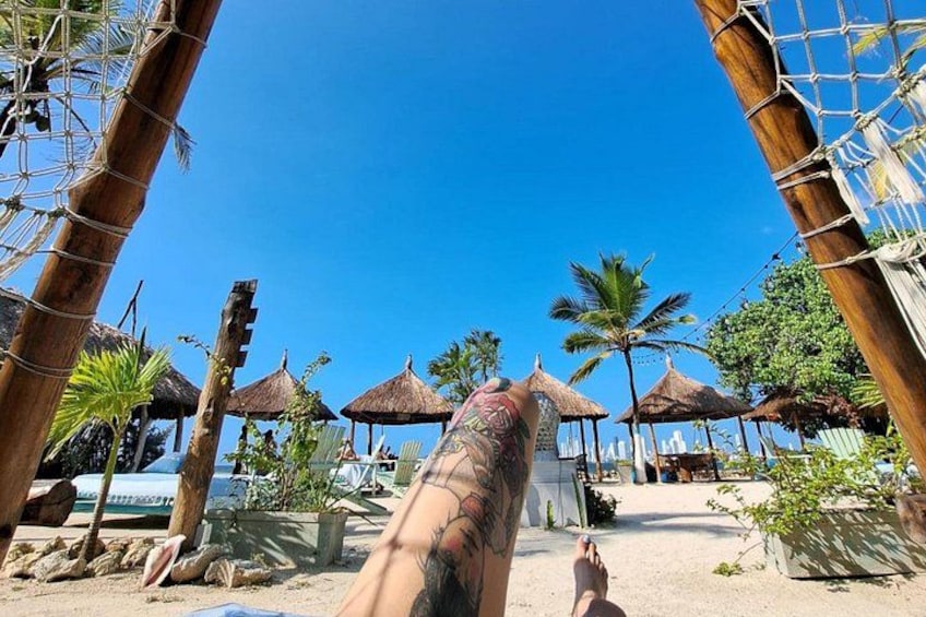 Een strand met rieten parasols, palmbomen en een helderblauwe lucht. 2