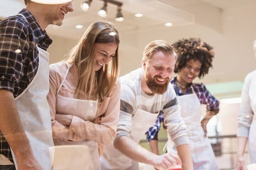 A group of people in a kitchen, some wearing aprons, engaged in cooking or food preparation activities. 2