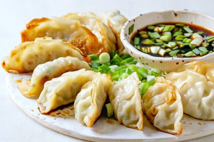 Un piatto di ravioli con salsa per intingere e cipollotto tritato. 1