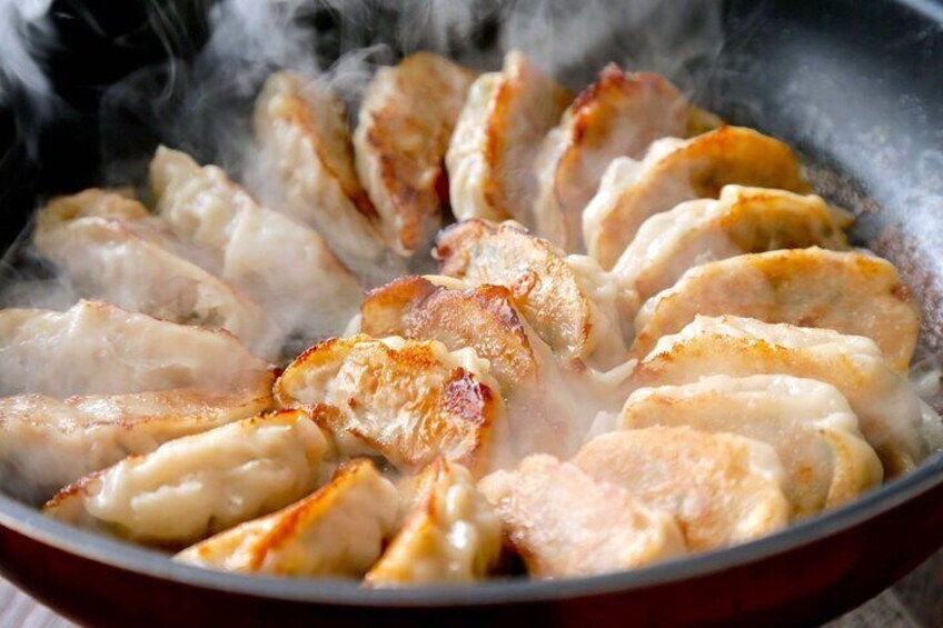 A pan with several pieces of meat cooking, steam rising from the pan. 4