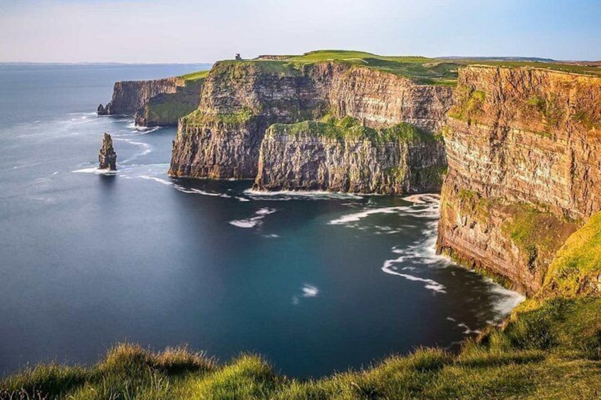 A coastal cliff with a lighthouse, a rocky outcrop, and a grassy cliff edge. 4