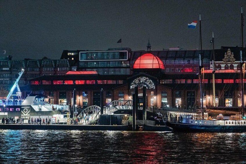A waterfront with a large illuminated building, a bridge, and a sailboat. 2