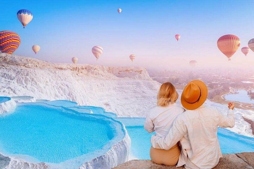 Una pareja sentada junto a una piscina turquesa con globos aerostáticos al fondo. 3