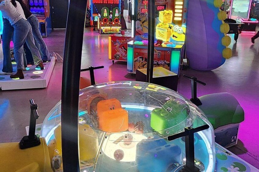 Un salón de juegos colorido con diversas máquinas recreativas y un área de juego transparente con un objeto amarillo y verde. 5