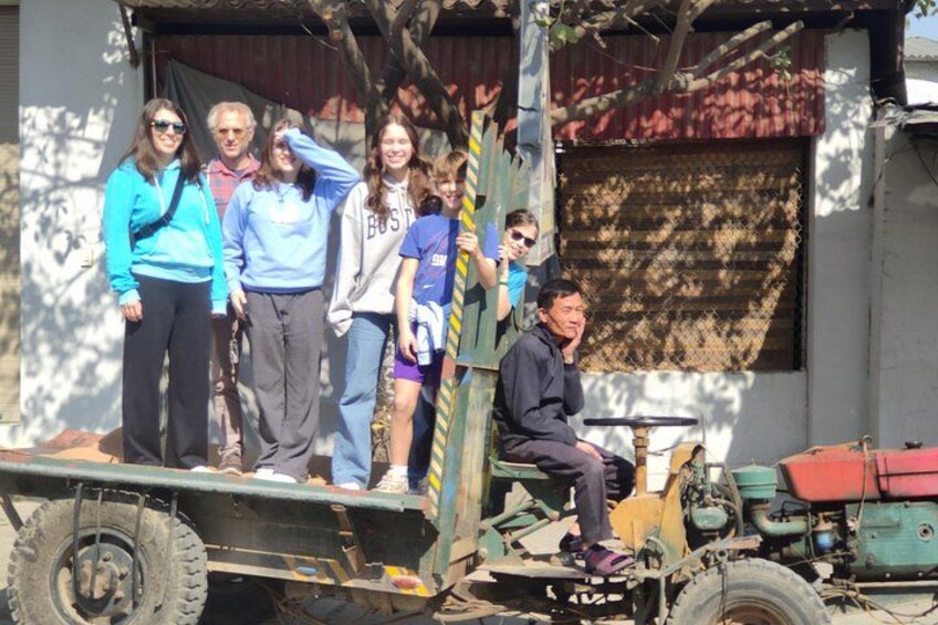 A group of people on a vehicle with a trailer, a tree, and a building in the background. 3