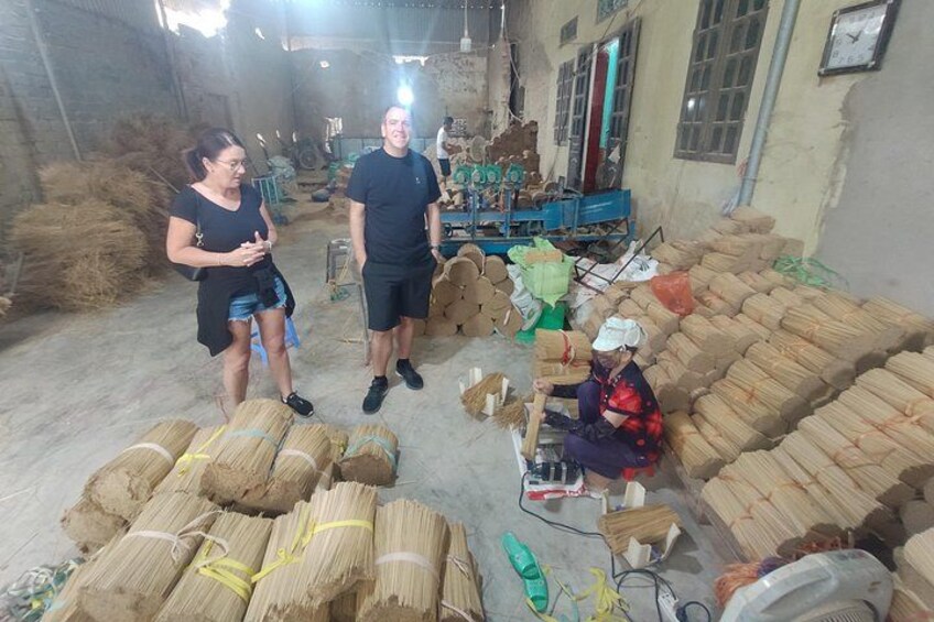 A warehouse with stacks of bamboo bundles, a person sitting on the floor, and another person standing and talking. 5
