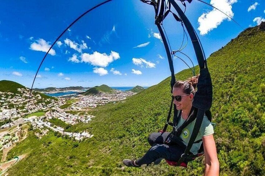 A person on a cable car over a lush green landscape with a view of a coastal town below. 3