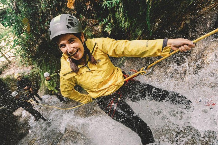 A person rappelling down a rocky cliff, wearing a helmet and a yellow jacket. 5