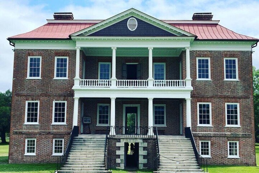 A large brick building with a central porch, two staircases, and a red roof. 1