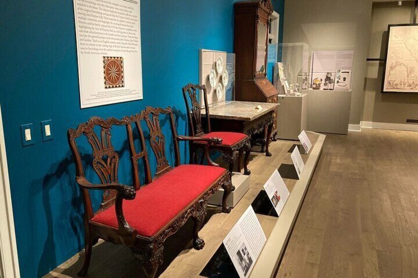 Antique wooden chairs with red cushions and a display table in a museum. 2