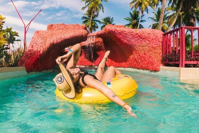 A person floating on a yellow inflatable tube in a pool with red rock formations and palm trees in the background. 4