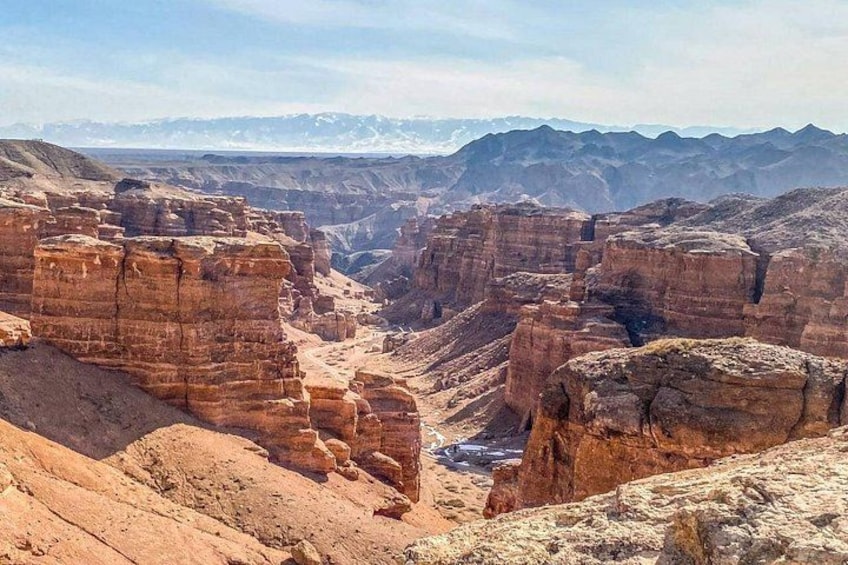 Un canyon aux formations rocheuses en strates, avec des montagnes qui se dessinent à l’horizon. 2