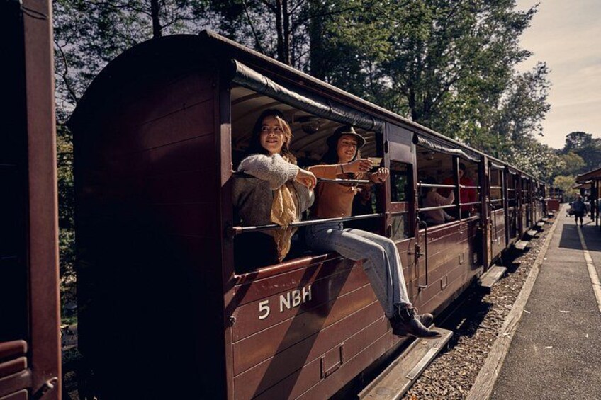 A vintage train with passengers, number 5 NSH, on a track with a platform and trees in the background. 2