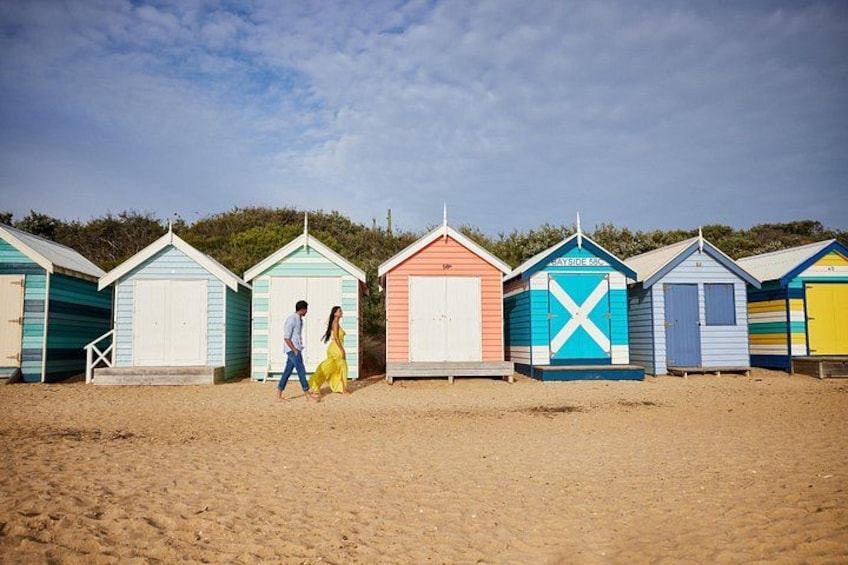 A row of colorful beach huts with a couple walking in front. 2