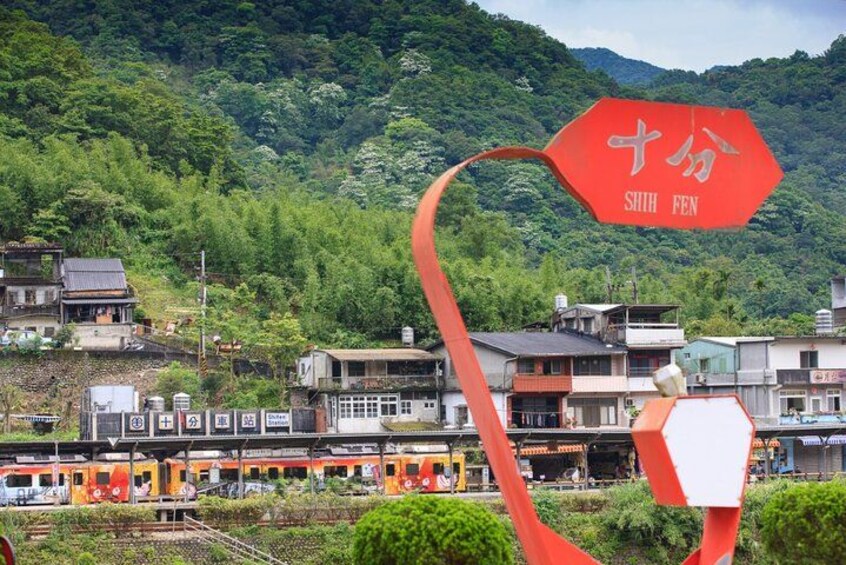 A red kite with 'SHIH FEN' written on it, a train, and a mountainous landscape with buildings. 2