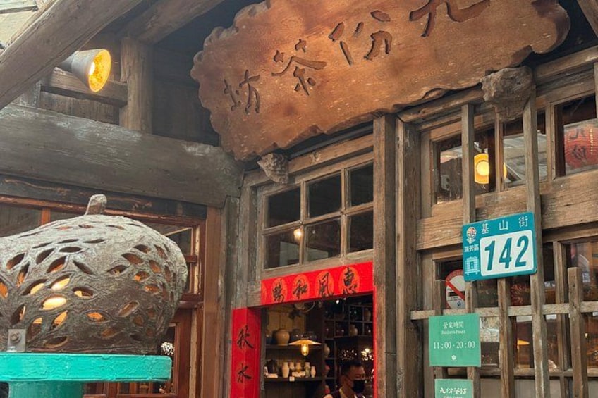 A traditional wooden building with a signboard, a hanging lantern, and a storefront with a red sign. 3