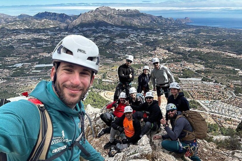 En grupp människor med hjälmar och ryggsäckar står på en bergstopp och har utsikt över en stad nedanför. 1