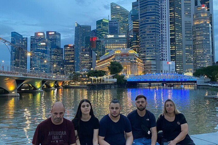 A group of people sitting by a river with a city skyline in the background. 5