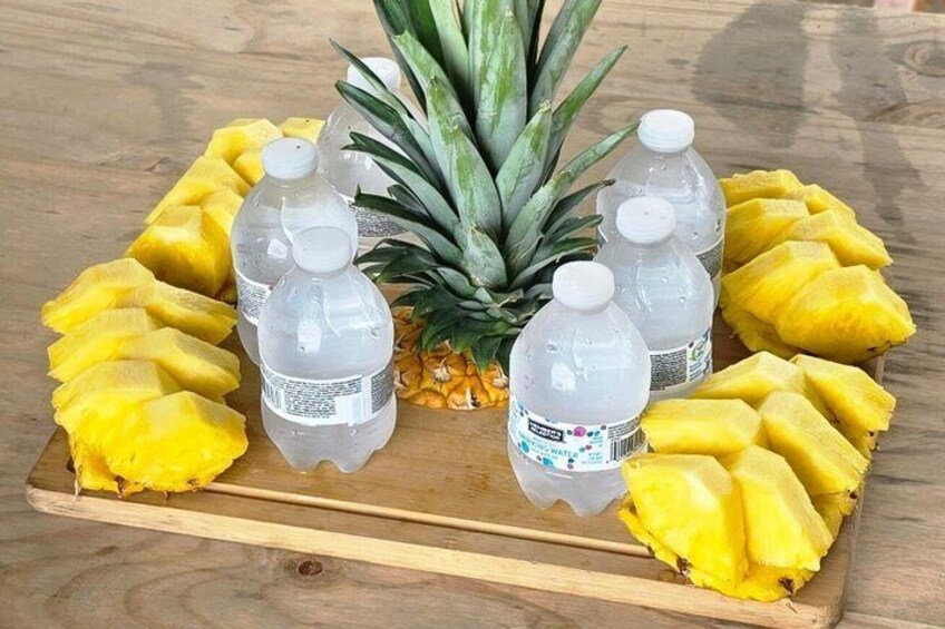 A wooden tray with sliced pineapples and plastic bottles of water. 2
