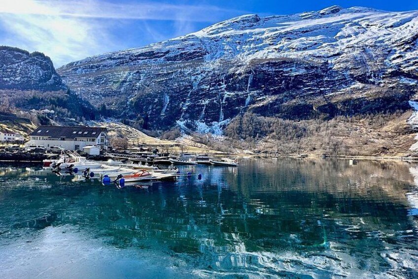 A frozen lake with boats, a small settlement, and snow-covered mountains. 4
