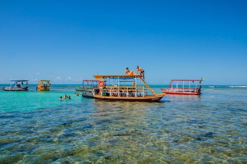A clear blue sea with several boats, including a large yellow boat with people on it. 5