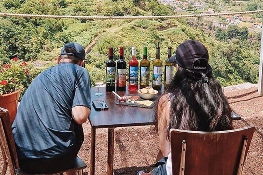 Due persone sedute a tavola con bottiglie di vino e stuzzichini, con vista su un vigneto. 5