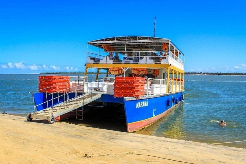 A blue and yellow ferry named 'MARANA' docked at a sandy beach with calm water. 2