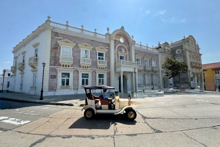 Ein historisches Gebäude mit aufwendiger Architektur, ein geparktes Oldtimer-Auto und ein strahlend blauer Himmel. 3