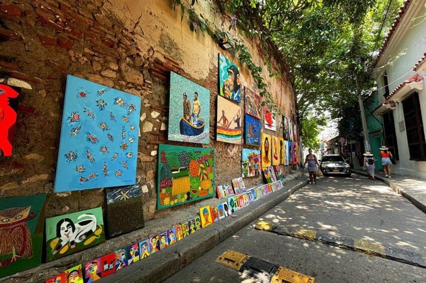 A street with colorful murals on a brick wall, a sidewalk with painted tiles, and a car parked on the road. 4