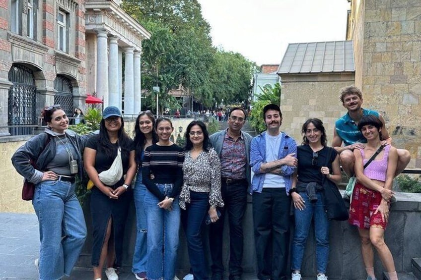 A group of people posing in an urban setting with historical architecture and a stone wall. 3