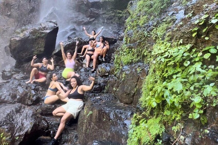A group of people sitting on rocks near a waterfall. 2