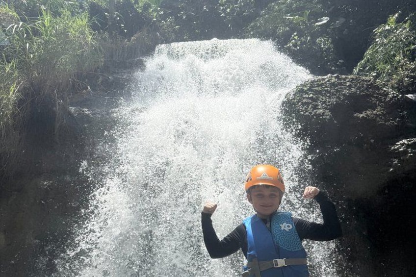 A person in a helmet and life vest standing in front of a waterfall. 4