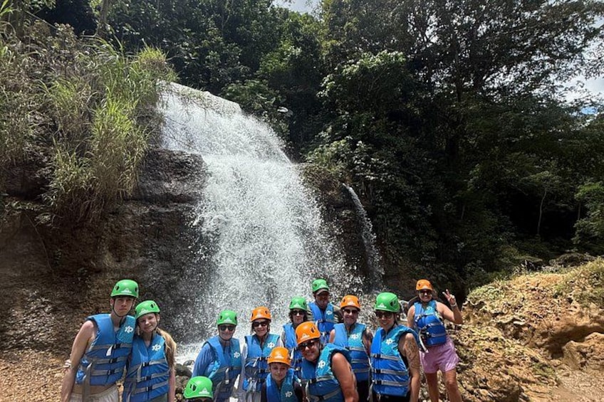 A group of people in blue life jackets and helmets posing in front of a waterfall. 3