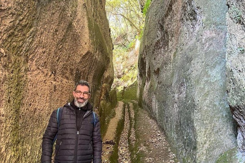 A person standing between two large rock formations in a narrow canyon with a stream running through. 1