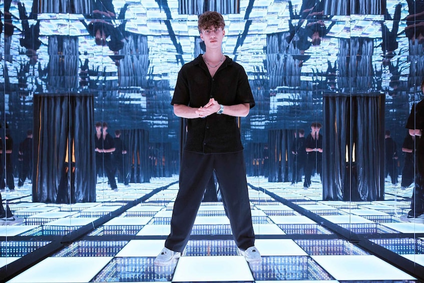 A person standing on a reflective floor with a grid pattern, surrounded by mirrored walls. 2