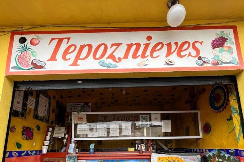 A fruit stand named 'Tepoznieves' with a colorful signboard and various fruits displayed inside. 4
