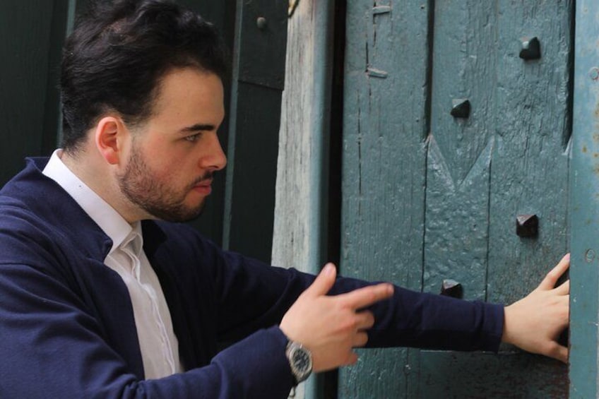A man in a suit leaning on a green door with a watch on his wrist. 4