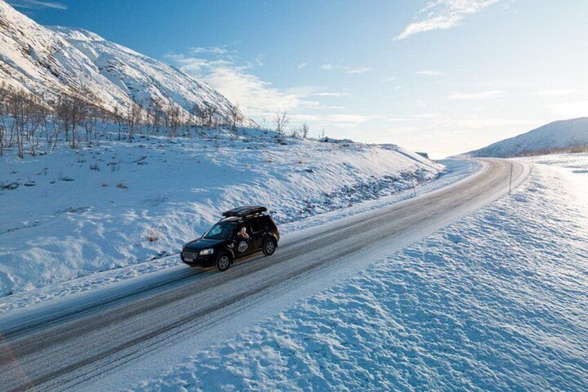 Un SUV negro en una carretera nevada con montañas al fondo. 3
