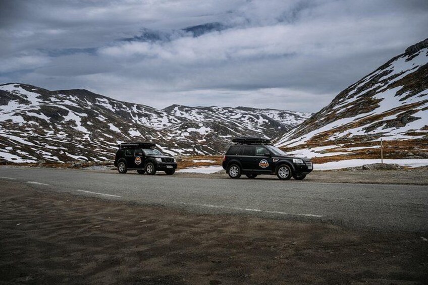 Two vehicles on a road with snow-covered mountains in the background. 3