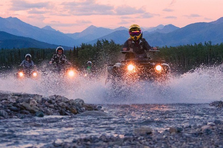 Three people on all-terrain vehicles (ATVs) riding through a shallow water crossing. 1