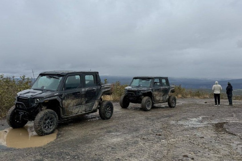 Two off-road vehicles parked on a muddy terrain with a person standing in the background. 4