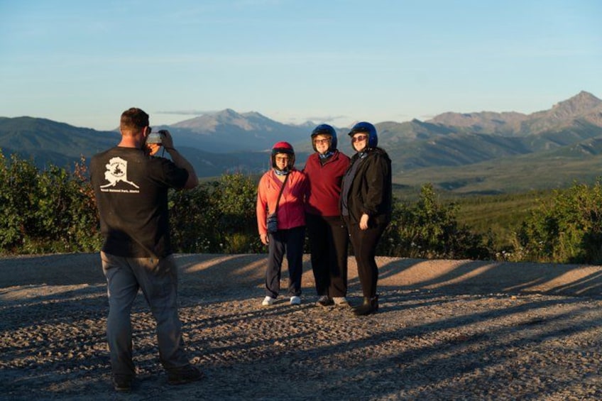 A group of people standing on a gravel path with a mountainous landscape in the background. 5