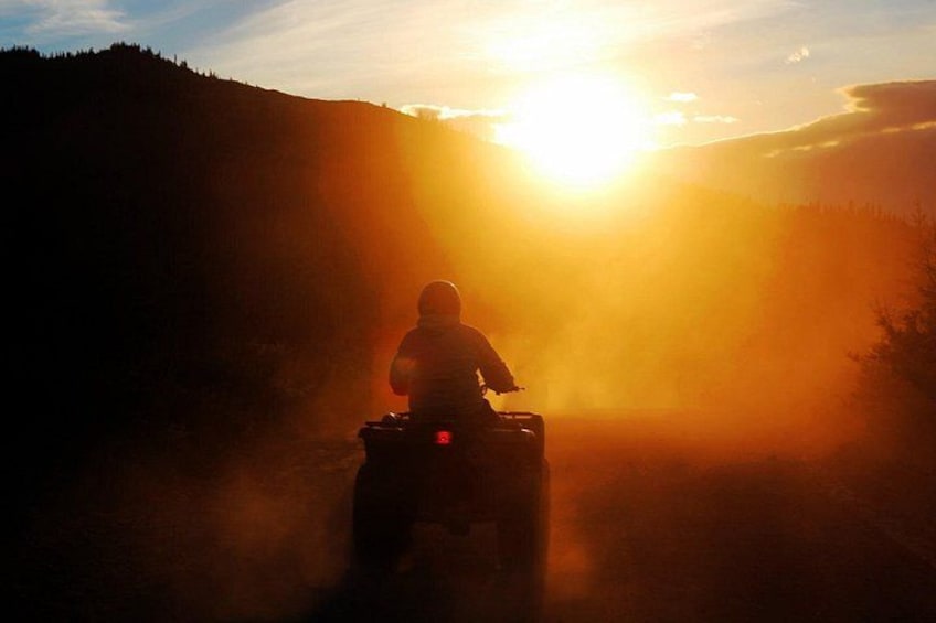 A person riding an ATV on a road with a sunset in the background. 4
