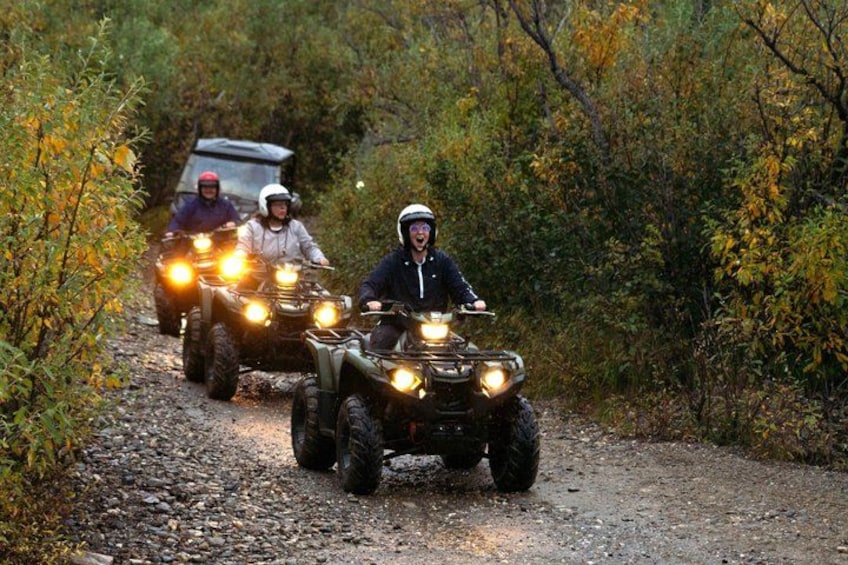 Three people riding ATVs on a dirt path surrounded by trees. 2