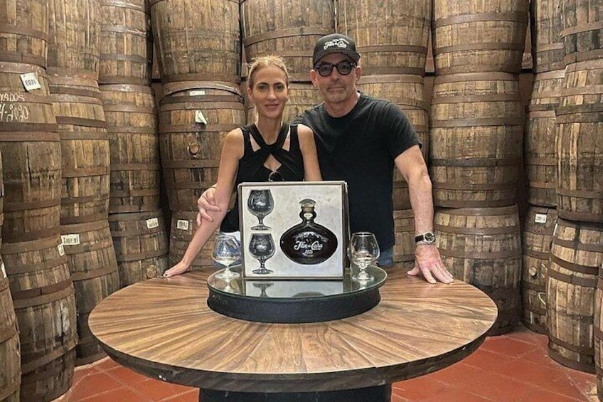 Two people standing in a wine cellar with wooden barrels in the background. 3