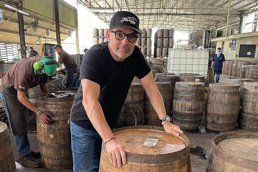 A person leaning on a wooden barrel in a warehouse filled with barrels. 5