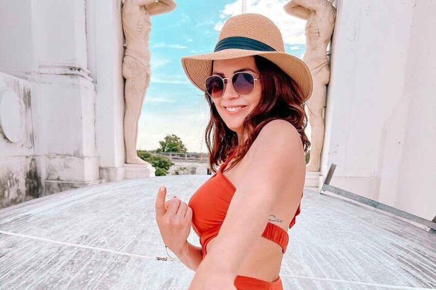 A person in a red swimsuit and straw hat standing on a white tiled floor with statues in the background. 3