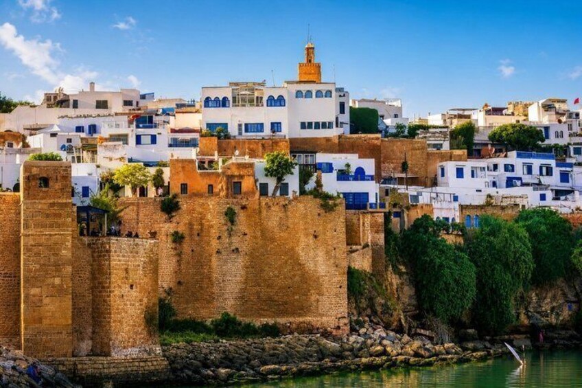 A coastal town with white and blue buildings, a large stone wall, and a clear blue sky. 1